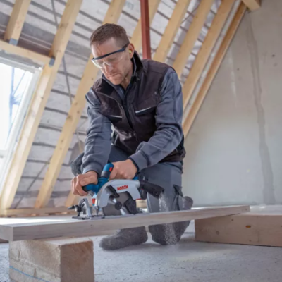 Homem usando serra circular elétrica para cortar madeira num local de construção