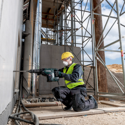 Homem com equipamento de proteção a usar furadeira numa obra com andaimes