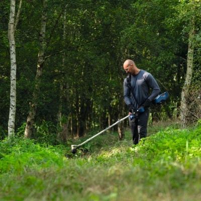 Homem a aparar relva numa área verde com aparador elétrico azul