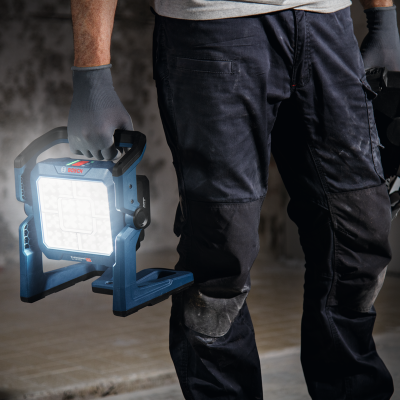 Lanterna de trabalho portátil azul e preta Bosch com LED segurada por trabalhador com calças pretas e luvas cinza