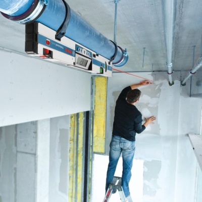Homem numa escada a trabalhar numa parede branca com cano azul e nivel de bolha no tecto