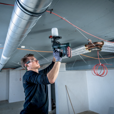 Homem a usar equipamento elétrico para reparação no teto com tubagem e fios expostos