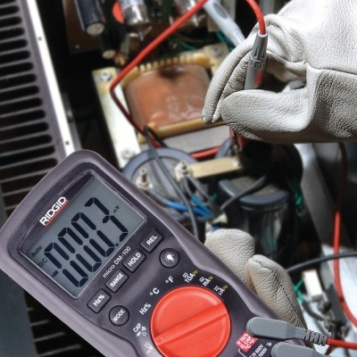 Multímetro digital RIDGID DRO20 medindo tensão de 100,3V em painel elétrico.