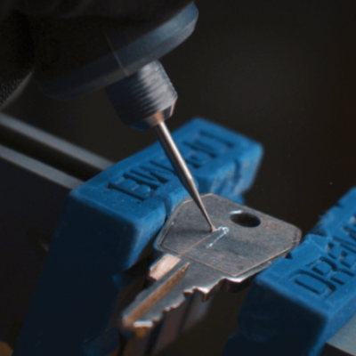 Chave metálica presa numa morsa azul com texto DREAMZ e ferramenta de precisão a gravar