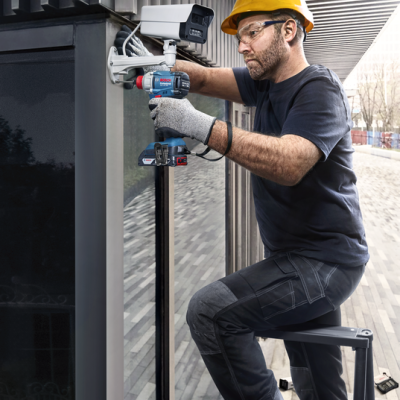 Homem com capacete amarelo instalando câmara de segurança numa parede de vidro