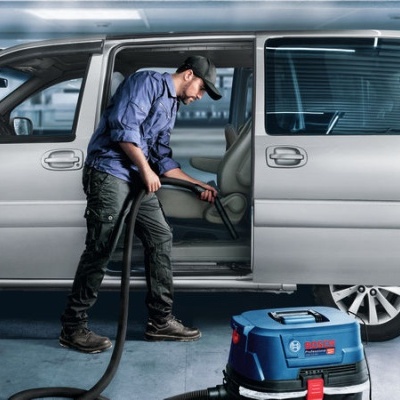 Homem a aspirar o interior de uma carrinha cinzenta com máquina de aspiração azul.