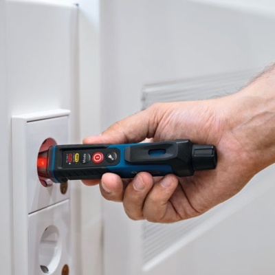 Dispositivo de teste elétrico azul e preto em tomada branca junto a radiador