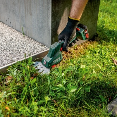 Cortador de relva sem fio a aparar relva junto a uma parede de cimento