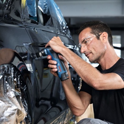 Homem repara carro preto com ferramenta elétrica numa oficina