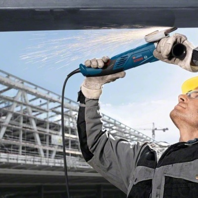 Homem com capacete amarelo usa ferramenta elétrica Bosch para cortar metal