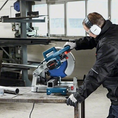 Serra elétrica de mesa azul e preta em uso por homem em ambiente industrial