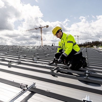 Trabalhador a instalar painéis solares num telhado de metal cinzento