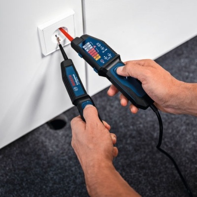 Ferramentas de teste elétrico a trabalhar numa tomada numa parede branca