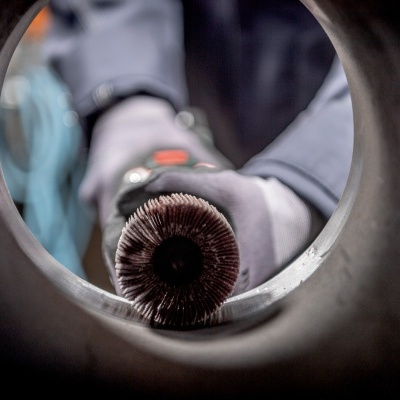 Vista interna de tubo metálico com escova circular giratória segurada por mão com luva