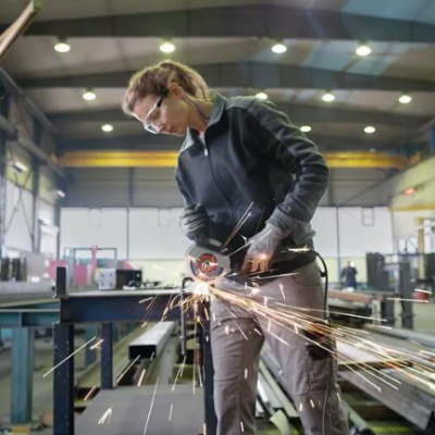 Pessoa com óculos de proteção usando rebarbadora elétrica para cortar metal numa fábrica