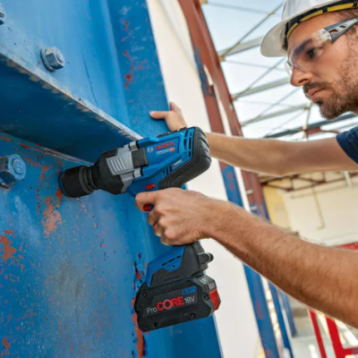 Parafusadeira Bosch azul escuro a ser usada por operário com capacete branco numa estrutura metálica azul