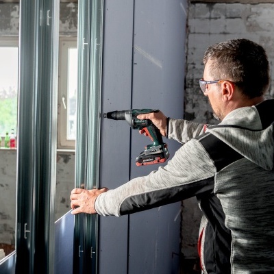 Homem a montar estrutura metálica com ferramenta elétrica em espaço interior