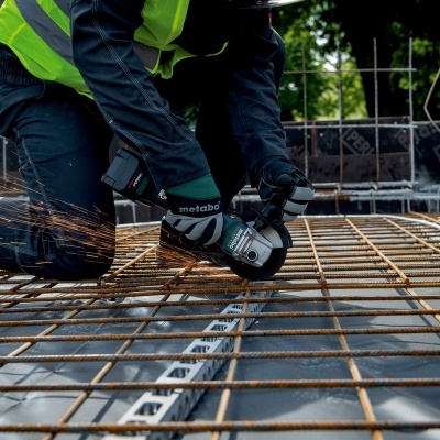 Pessoa a usar esmerilhadora elétrica Metabo na construção sobre vergalhões de aço