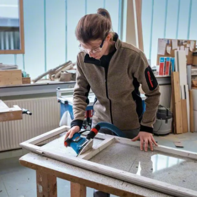Pessoa a usar ferramenta elétrica para trabalhar moldura de madeira branca numa oficina