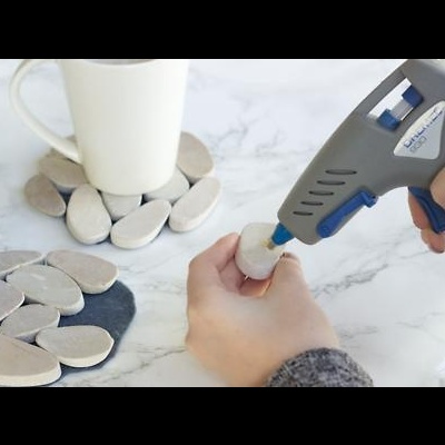 Colher para pistola de cola quente a aplicar cola em pedra, perto de pedras e caneca branca num tampo.