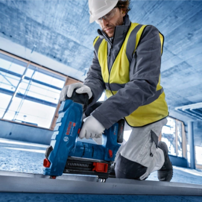 Trabalhador da construção com equipamento de proteção a usar pistola de pregos Bosch azul e vermelha