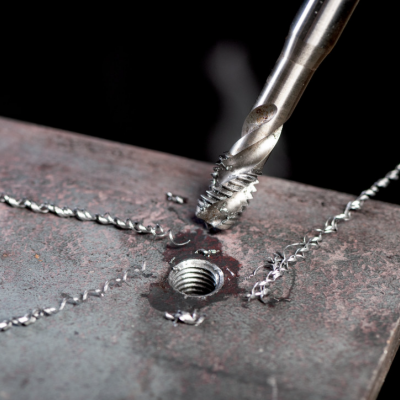 Broca metálica a processar parafuso em chapa de metal escura com cavaco espiralado