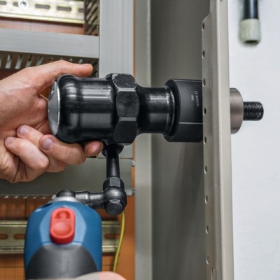 Pessoa usando ferramenta preta em porta metálica cinza com ferramenta elétrica azul e preta ao fundo