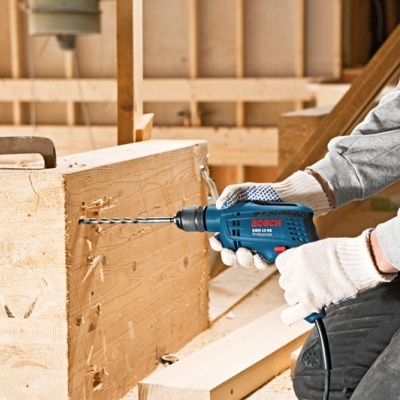 Pessoa a usar furadeira Bosch numa estrutura de madeira interior