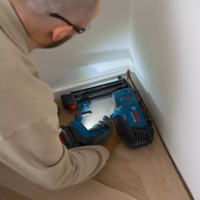 homem a instalar tomada numa parede branca com ferramentas Bosch azuis no chão de madeira clara