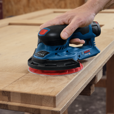 Lixadora Bosch Professional azul e preta com disco vermelho em madeira clara numa oficina