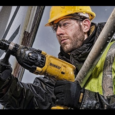 Homem com capacete amarelo e colete refletor segurando uma furadeira DEWALT em ambiente molhado