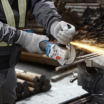 Pessoa a usar luvas e roupa de proteção a cortar barra de metal com esmerilhadora numa oficina