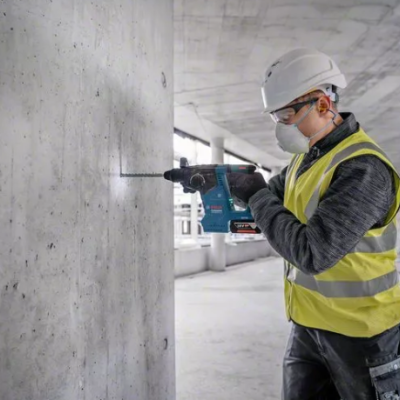 Homem com capacete e colete perfurando coluna de cimento em obra