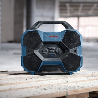 Aparelho de som portátil Bosch preto e azul num palete de madeira num ambiente industrial