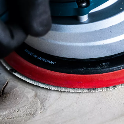 Lixadora elétrica circular com base vermelha e texto 'MADE IN GERMANY' em madeira clara