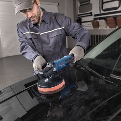 Homem a polir capot de carro preto com polidora elétrica