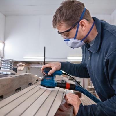 Homem a lixar madeira com lixadora elétrica numa oficina
