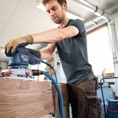 Homem a lixar superfície de madeira com lixadora elétrica em oficina