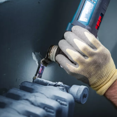 Mão com luva a usar ferramenta elétrica para trabalhar uma parede cinza