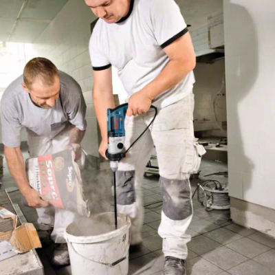 Dois homens misturam material de construção num balde num ambiente de obra.