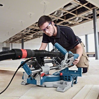 Homem a usar serra de esquadria azul a cortar madeira num espaço em construção