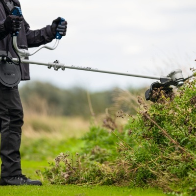 Pessoa a usar máquina desbastadora num campo verde com céu nublado