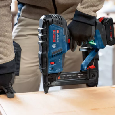 Pessoa usando ferramenta elétrica Bosch azul e preta para pregar madeira clara