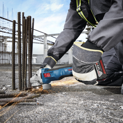 Pessoa a usar equipamento de proteção a cortar barras de aço com ferramenta elétrica Bosch azul num canteiro de obras