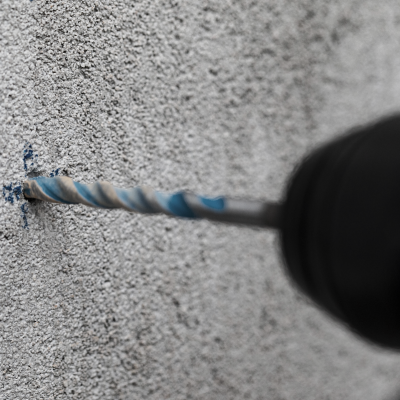 Broca perfurando parede granulado cinza com marcas azuis