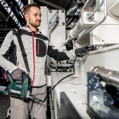 Homem com roupa de trabalho a usar ferramenta eléctrica junto a máquina industrial