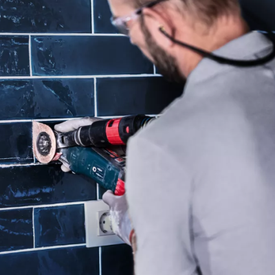 Pessoa a furar azulejos azuis numa parede com ferramenta elétrica
