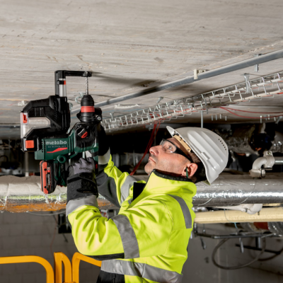 Trabalhador com capacete e casaco de alta visibilidade a usar ferramenta elétrica Metabo no teto