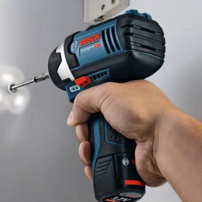 Pessoa a usar parafusadeira elétrica Bosch preta e azul a perfurar uma parede branca.