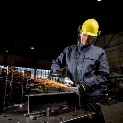 Homem com capacete amarelo e roupa de proteção a usar esmerilhadora em oficina escura